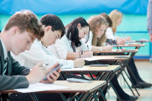 A group of students sitting at their desks looking at their phones.