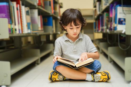 A young boy sitting on the floor reading a book.