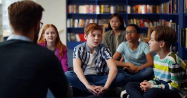 A group of people sitting in front of a book shelf.