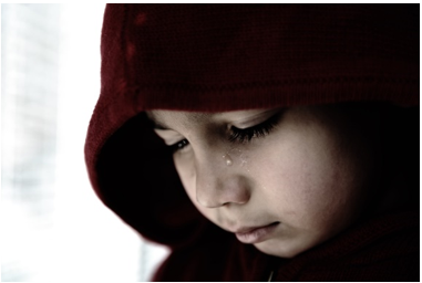 A young child wearing a hooded jacket and looking down.