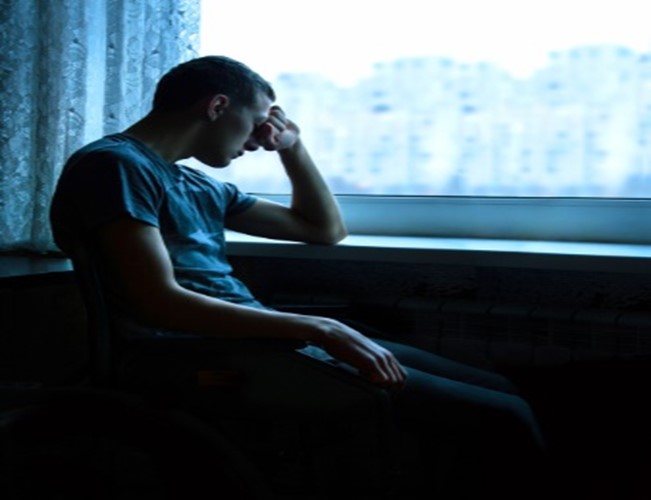 A man sitting in front of a window with his head down.