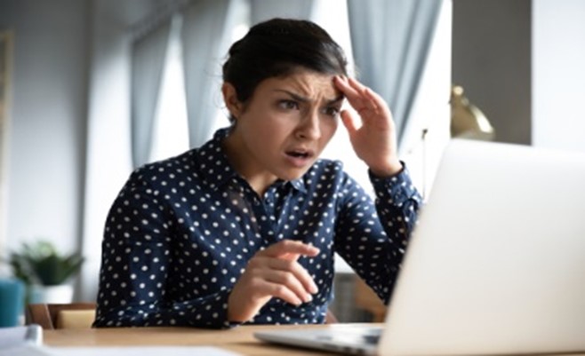 A woman is looking at her laptop with an angry look on her face.