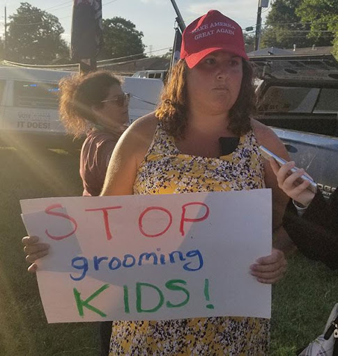 A woman holding up a sign that says stop grooming kids.