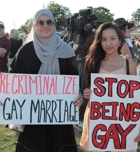 Two women holding signs that say " stop being gay ".