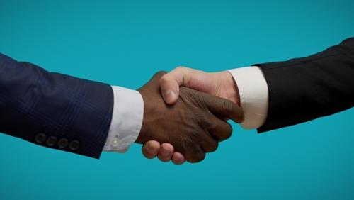 Two people shaking hands in front of a blue background.