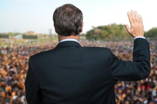 A man in a suit is waving at the crowd.