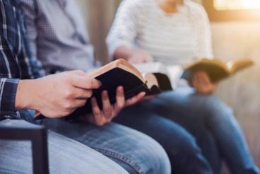 A man reading a book while sitting on someone 's lap.