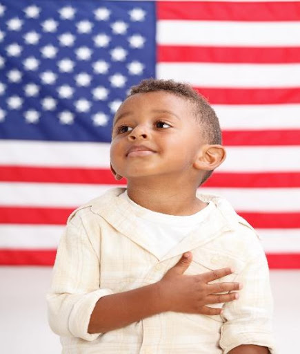 A young boy is standing in front of an american flag.