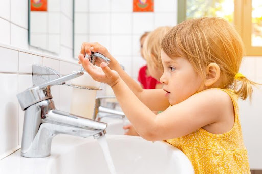 A little girl is washing her hands in the sink.