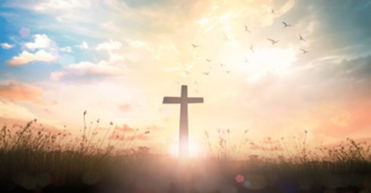 A cross in the middle of a field with birds flying above.