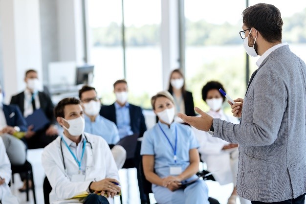 A group of people wearing masks and standing in front of a man.