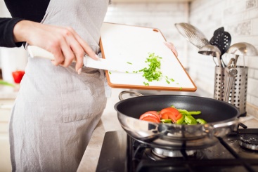 A person in an apron is cooking vegetables.