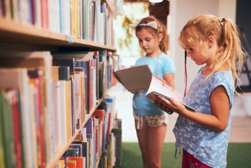 Two girls are looking at books in a library.