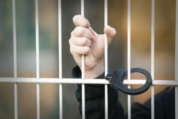 A person holding onto the bars of their jail cell.