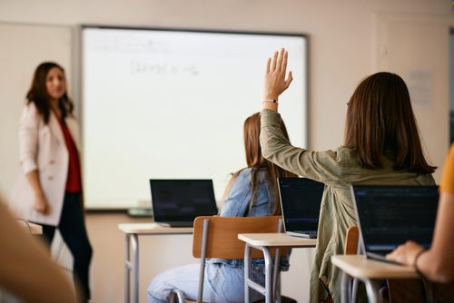 A woman raising her hand in front of an interactive whiteboard.